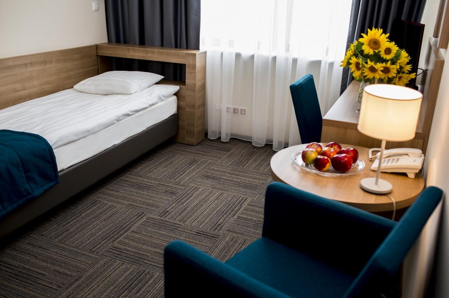 Przytulny pokój jednoosobowy z łóżkiem, biurkiem i fotelem ze stolikiem kawowym.