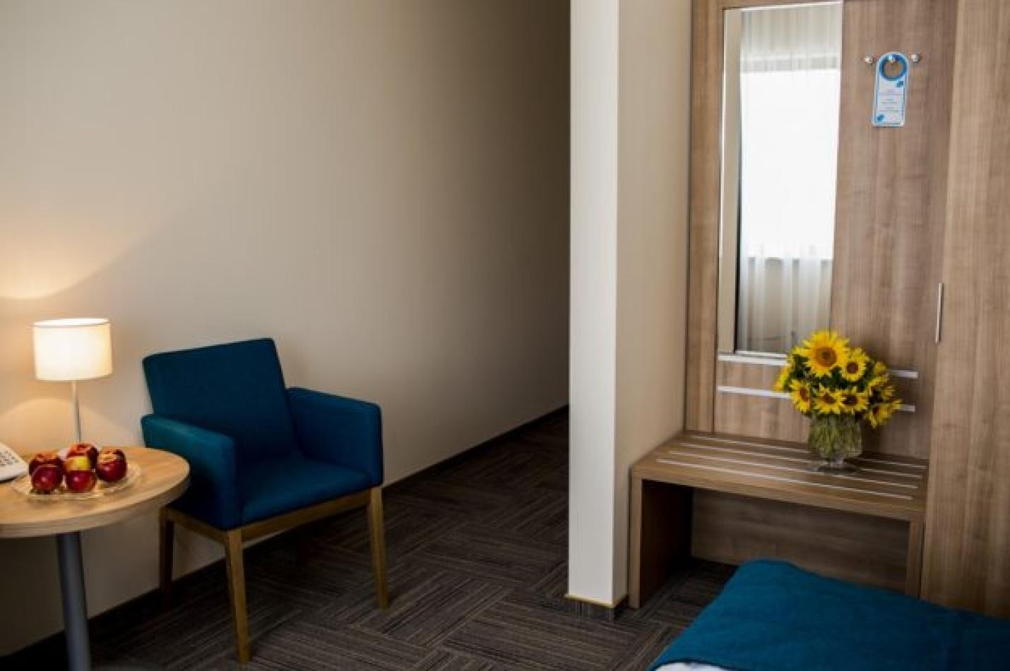 Nowoczesny pokój jednoosobowy z fotelem, stolikiem kawowym i zabudową z lustrem.