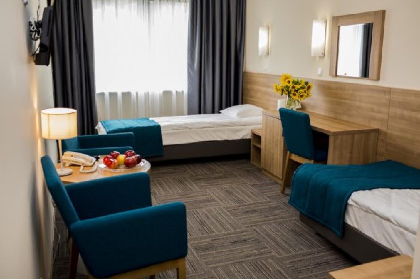 Pokój dwuosobowy z łóżkami, biurkiem oraz fotelami i stolikiem kawowym.