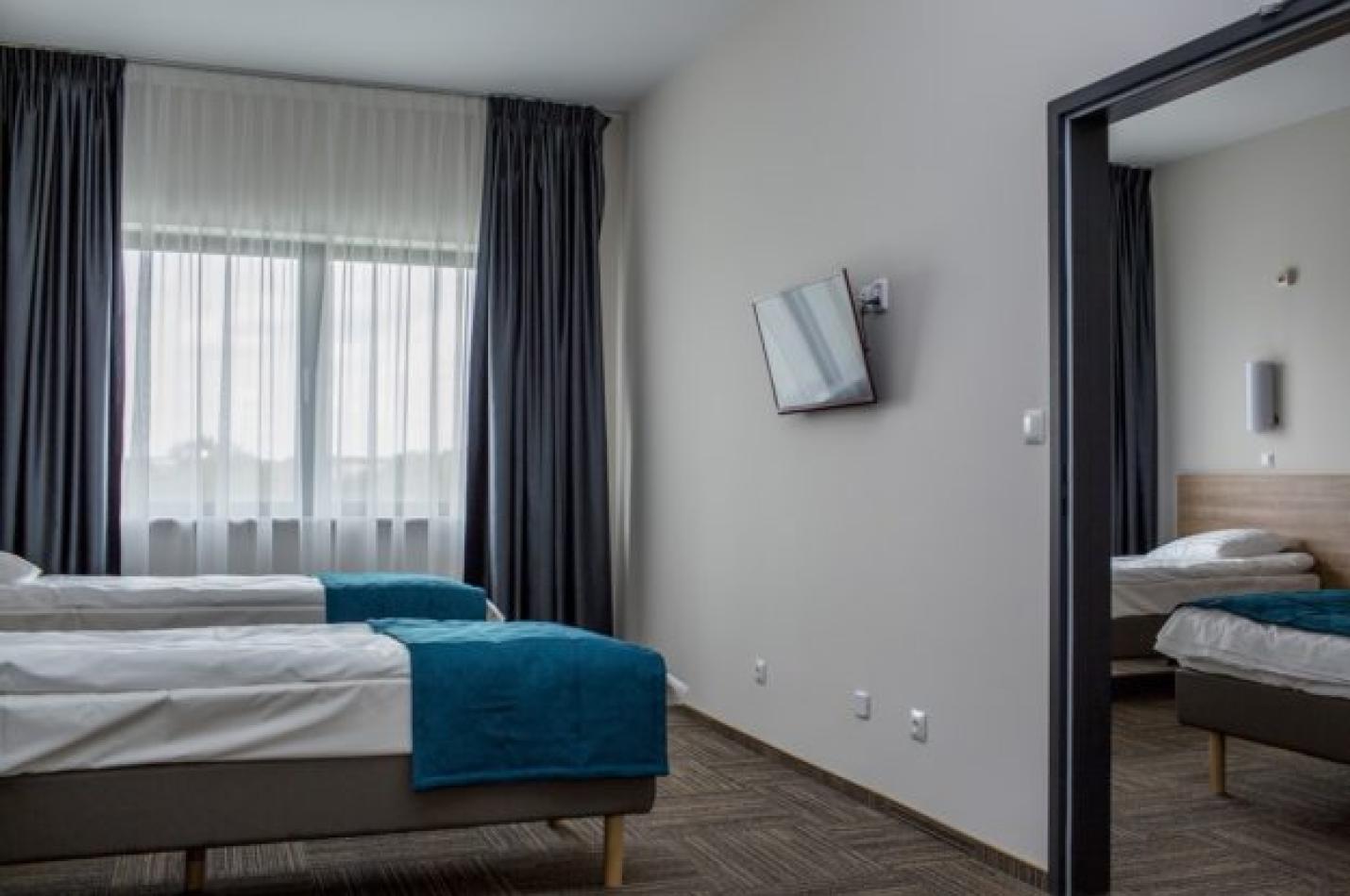 Pokój z dwoma łóżkami, telewizorem i przejściem do drugiej sypialni.