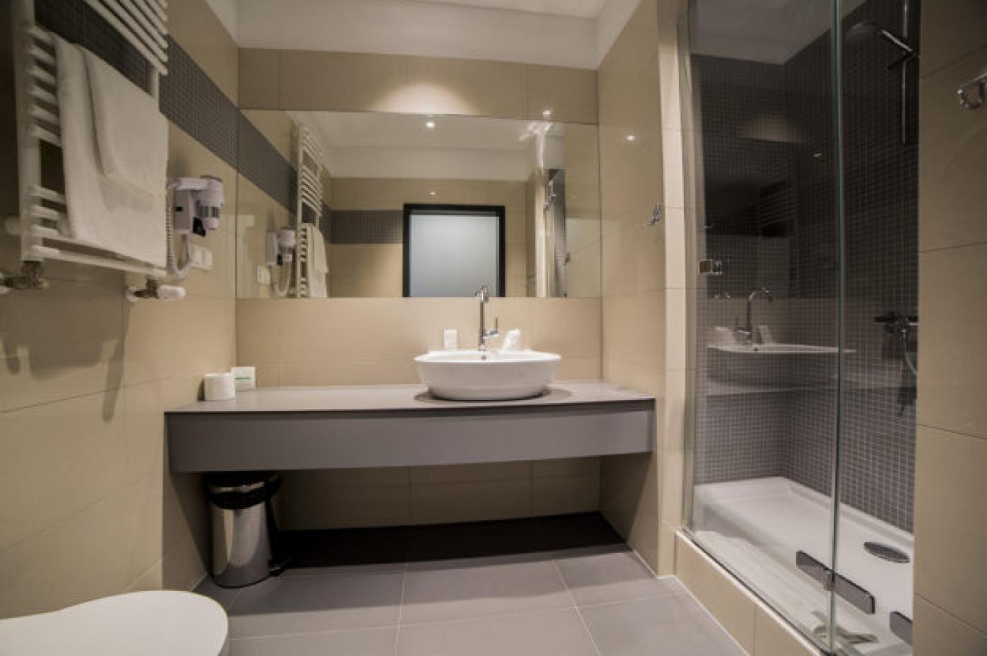 Nowoczesna łazienka z umywalką, dużym lustrem i przeszkloną kabiną prysznicową.