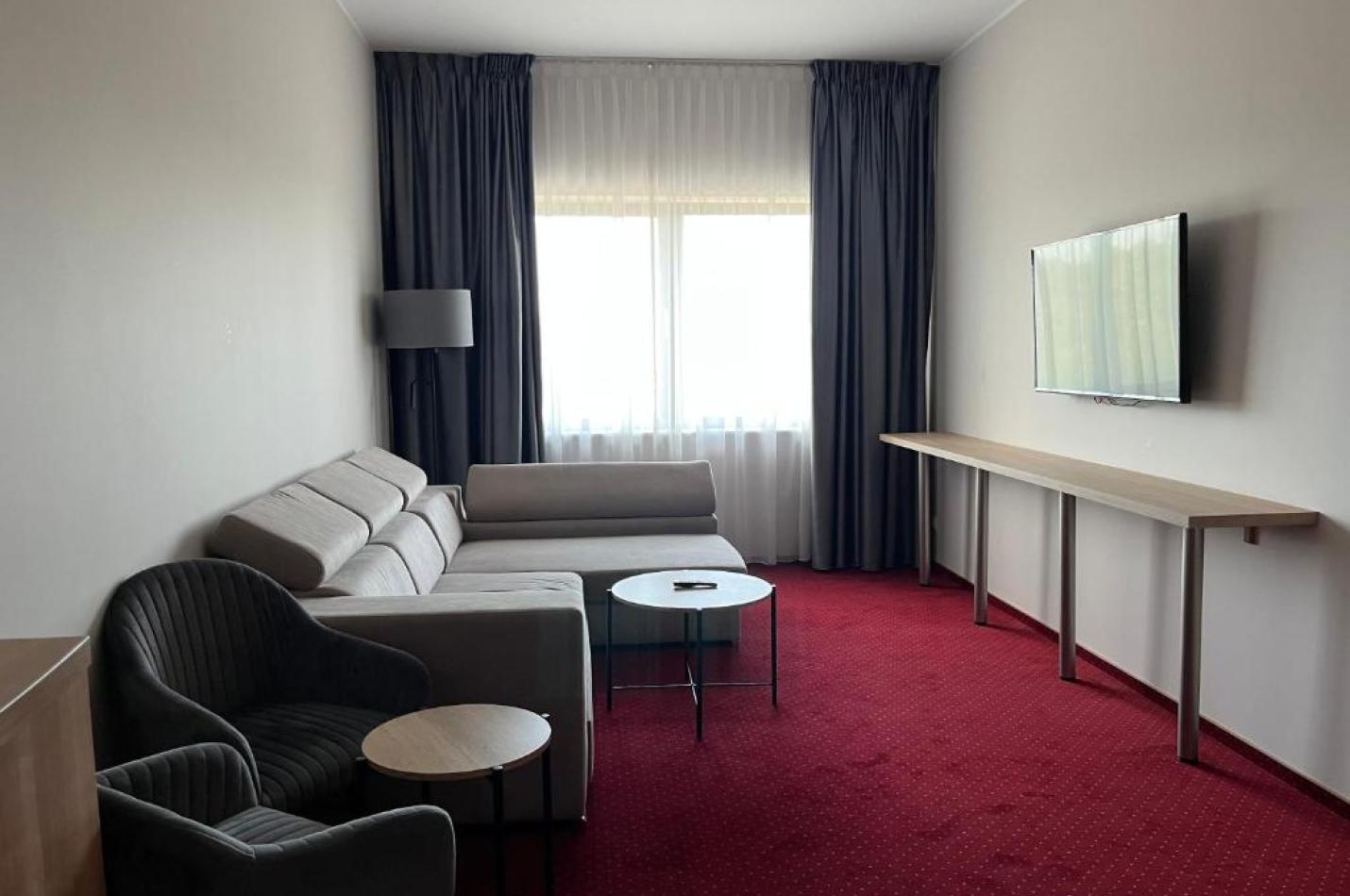 Duże pomieszczenie z kanapą, fotelami i stolikami kawowymi oraz telewizorem.