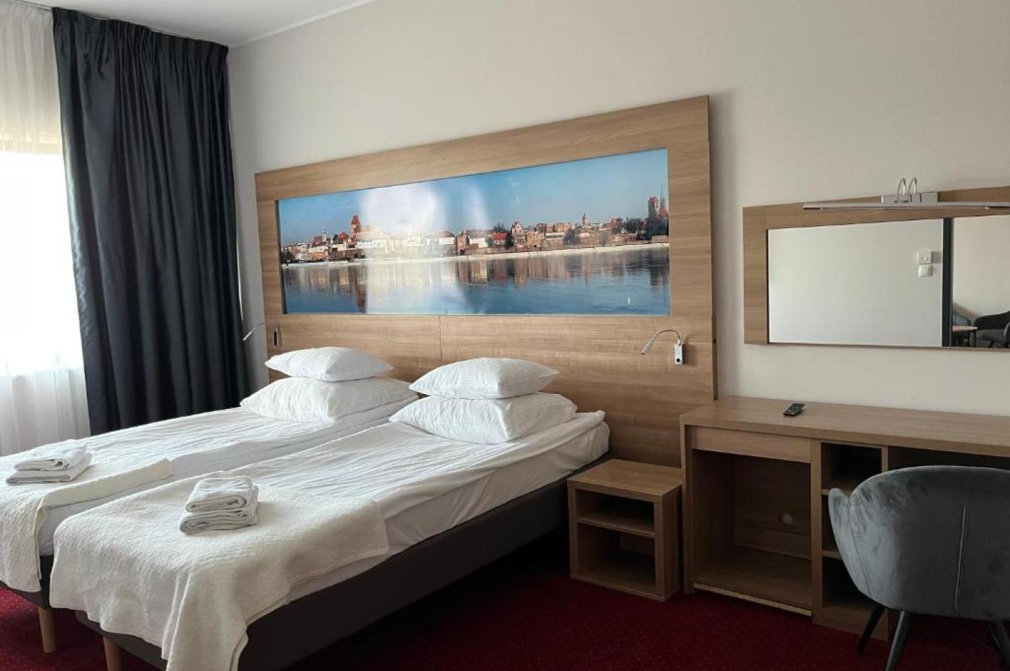 Sypialnia z dwoma łóżkami, biurkiem i fototapetą z panoramą miasta na ścianie.