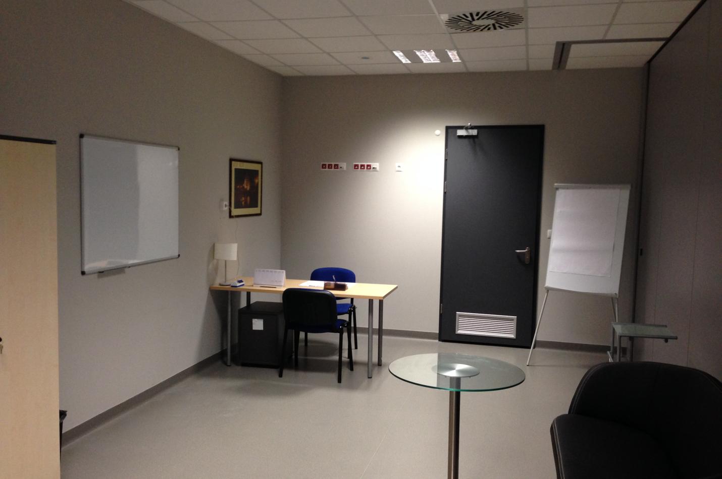 Minimalistyczne pomieszczenie z biurkiem i tablicami.