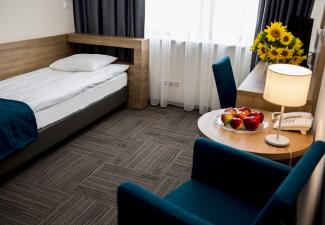 Przytulny pokój jednoosobowy z łóżkiem, biurkiem i fotelem ze stolikiem kawowym.