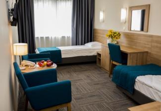 Pokój dwuosobowy z łóżkami, biurkiem oraz fotelami i stolikiem kawowym.