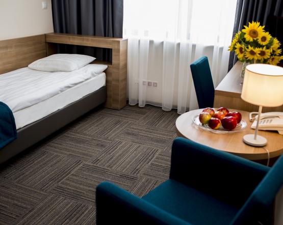 Przytulny pokój jednoosobowy z łóżkiem, biurkiem i fotelem ze stolikiem kawowym.