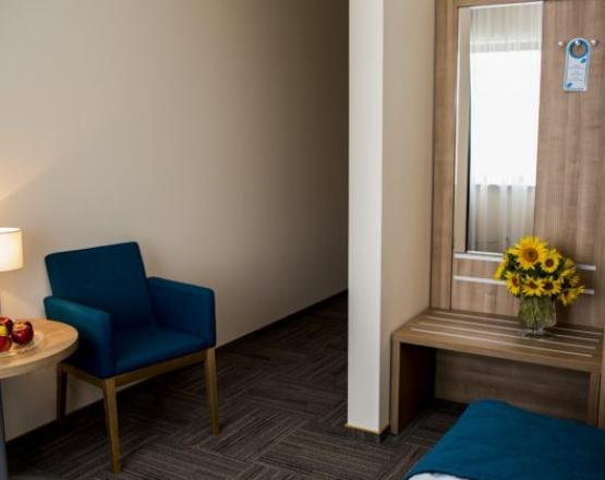 Nowoczesny pokój jednoosobowy z fotelem, stolikiem kawowym i zabudową z lustrem.