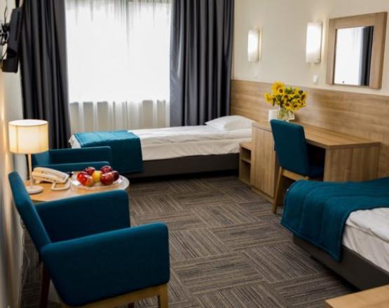 Pokój dwuosobowy z łóżkami, biurkiem oraz fotelami i stolikiem kawowym.