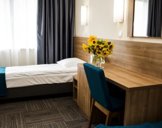 Łóżko pod oknem z szafką nocną, biurkiem i wazonem ze słonecznikami.