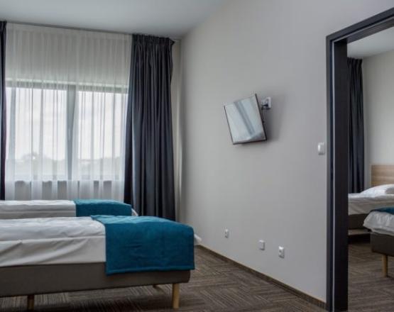 Pokój z dwoma łóżkami, telewizorem i przejściem do drugiej sypialni.