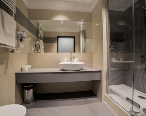 Nowoczesna łazienka z umywalką, dużym lustrem i przeszkloną kabiną prysznicową.