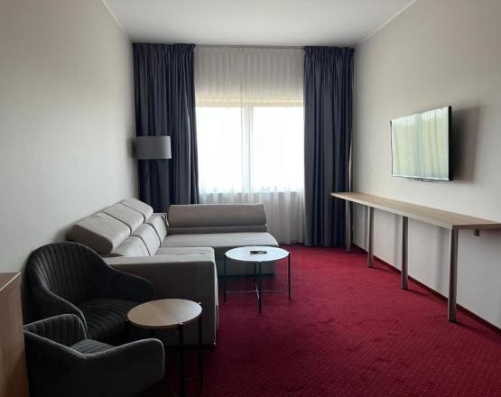 Duże pomieszczenie z kanapą, fotelami i stolikami kawowymi oraz telewizorem.