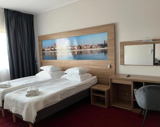 Sypialnia z dwoma łóżkami, biurkiem i fototapetą z panoramą miasta na ścianie.