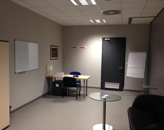 Minimalistyczne pomieszczenie z biurkiem i tablicami.