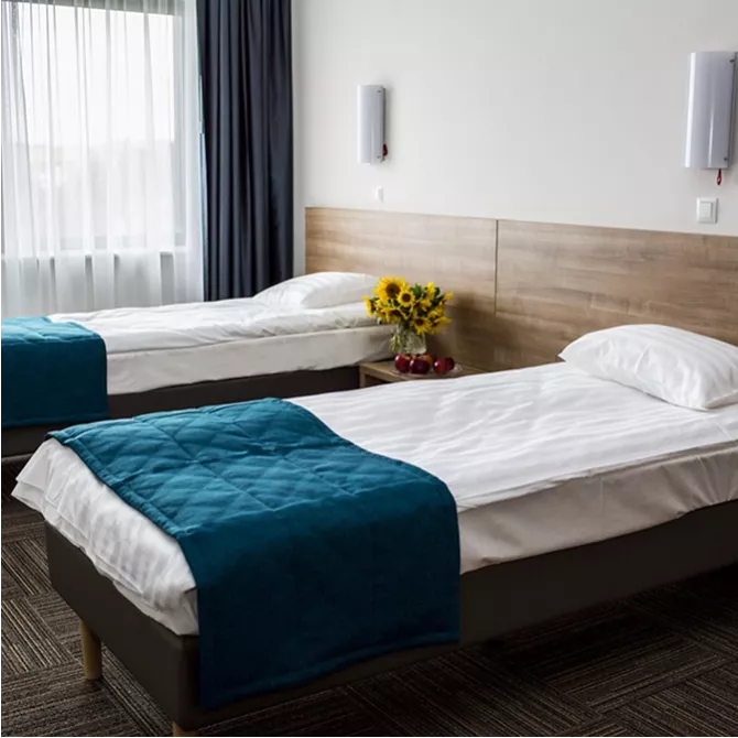 Świeżo pościelone łóżka hotelowe, a pomiędzy nimi wazon z kwiatami.