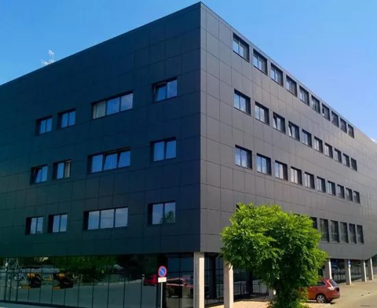 Nowoczesny czteropiętrowy budynek z przeszklonym parterem i dużymi oknami.